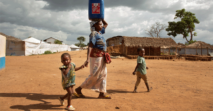 A woman carries a large jug of water through Gado refugee camp.