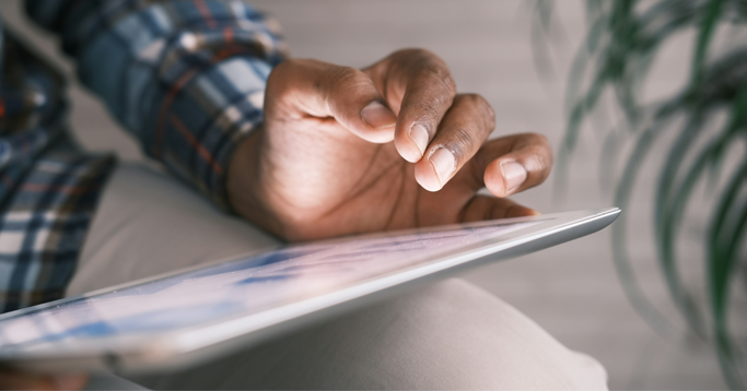 Photo of person in blue white and red plaid long sleeve shirt holding a computer tablet