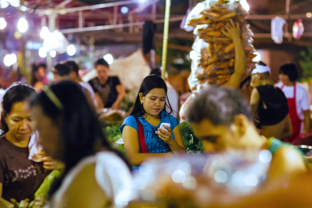 Photo of a young woman checking her smartphone in a busy Philippines market.