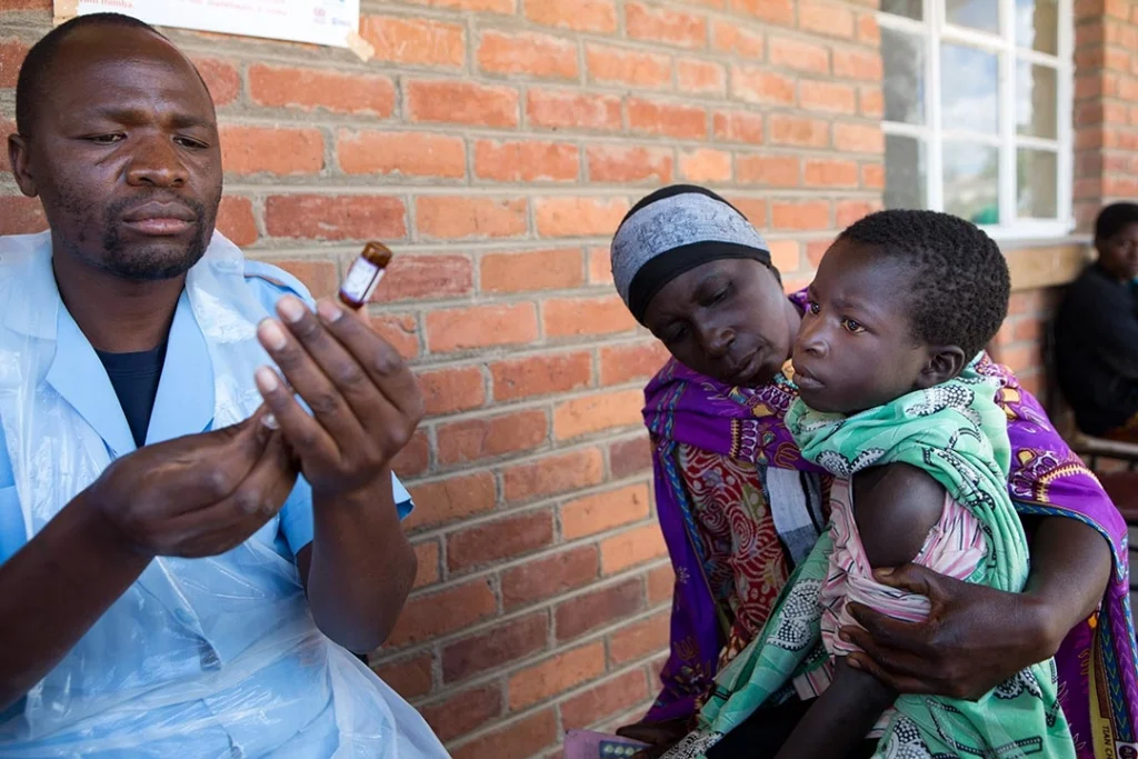 Photo of health worker preparing a vaccine injection for a waiting mother and child