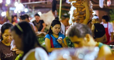 Photo of a young woman checking her smartphone in a busy Philippines market.