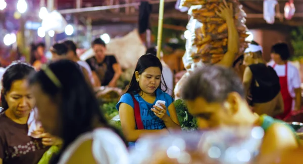 Photo of a young woman checking her smartphone in a busy Philippines market.