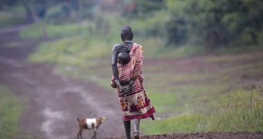 Photo of Suri Woman carrying a child while walking on a dirt road, Tulgit