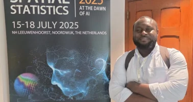 Photo of Dr Edson Utazi standing next to a Spatial Statistic 2025 conference poster