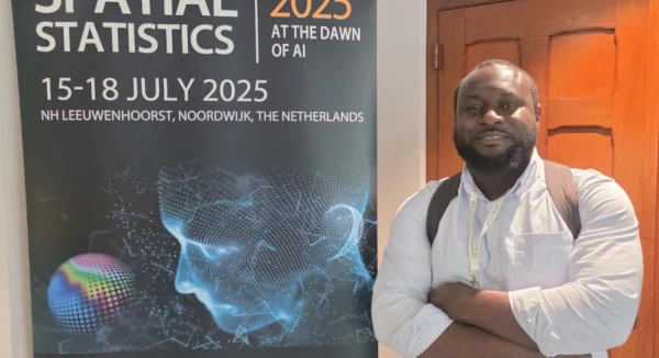 Photo of Dr Edson Utazi standing next to a Spatial Statistic 2025 conference poster