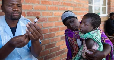 Photo of health worker preparing a vaccine injection for a waiting mother and child