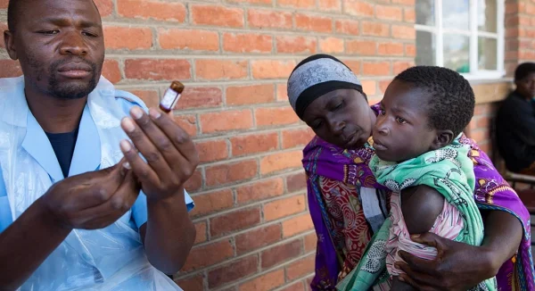 Photo of health worker preparing a vaccine injection for a waiting mother and child